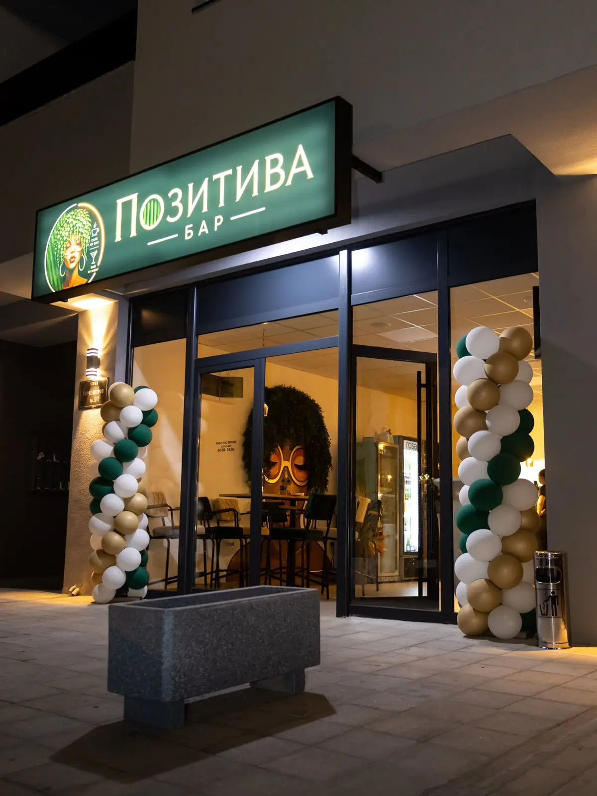 The Pozitiva Bar entrance at night, with the lit green sign and balloons from the opening